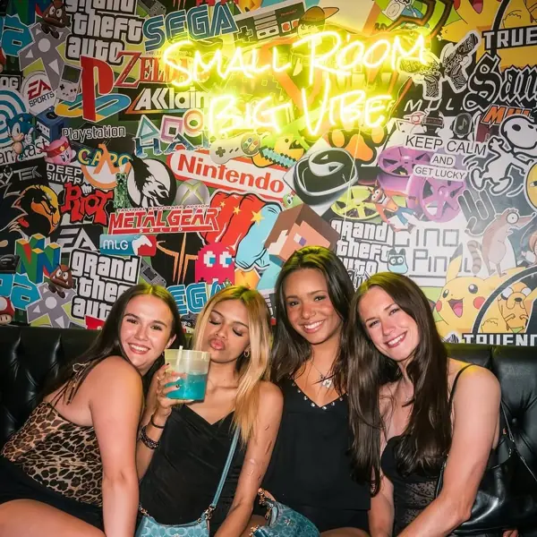 Friends posing under the neon 'Small Room Big Vibe' sign and graffiti mural